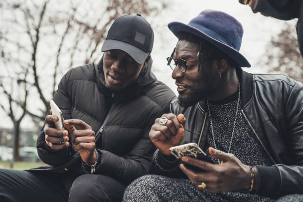 два африканских друга сидят на улице и смотрят в смартфон
 - Фото, изображение