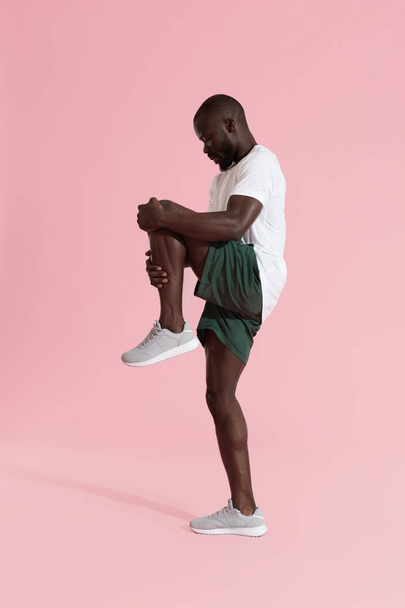 Man in sportswear stretching legs, warming up on pink background - Zdjęcie, obraz