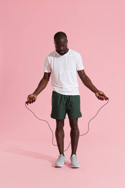 Sports man in sportswear with skipping rope on pink background - Фото, зображення