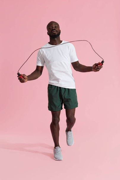 Sports man in sportswear with skipping rope on pink background - Valokuva, kuva