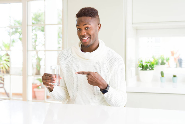 Uomo afroamericano che drizza un bicchiere d'acqua fresca molto felice indicando con mano e dito
 - Foto, immagini
