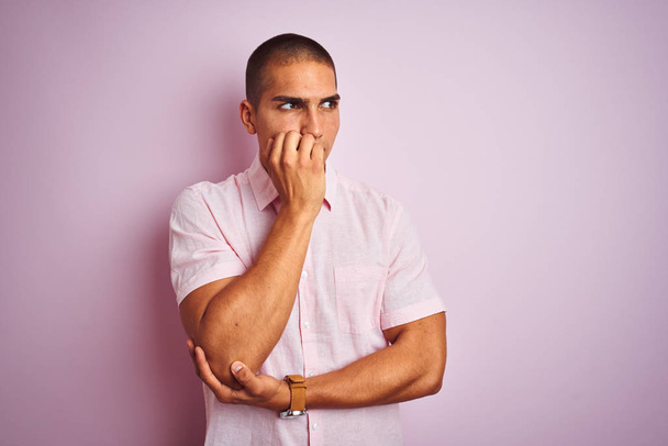 Jeune bel homme portant une chemise élégante sur fond rose isolé regardant stressé et nerveux avec les mains sur les ongles mordants de la bouche. Problème d'anxiété
. - Photo, image
