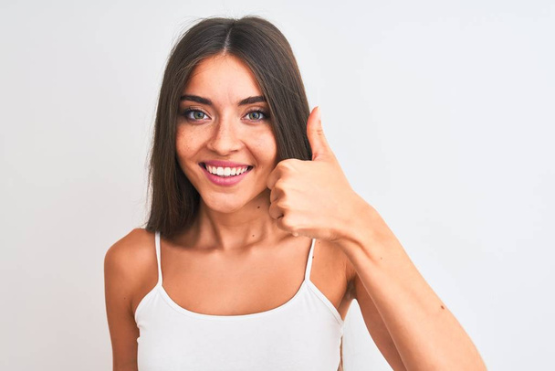 Молодая красивая женщина в повседневной футболке стоит на изолированном белом фоне счастливый с большой улыбкой делает хорошо знак, палец вверх пальцами, отличный знак
 - Фото, изображение