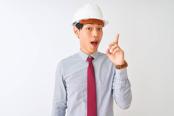 Chinese architect man wearing tie and helmet standing over isolated white background pointing finger up with successful idea. Exited and happy. Number one. - Φωτογραφία, εικόνα
