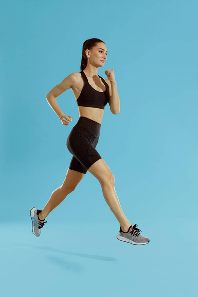 Sport woman with fit body jumping and running on blue background - 写真・画像