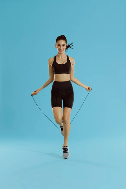 Fitness. Woman exercising with jumping rope on blue background - Φωτογραφία, εικόνα