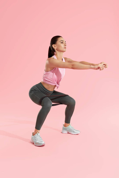 Squats. Woman in sports wear squatting with resistance band - Фото, зображення