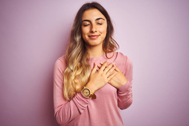 Young beautiful woman wearing a sweater over pink isolated background smiling with hands on chest with closed eyes and grateful gesture on face. Health concept. - Foto, Imagem