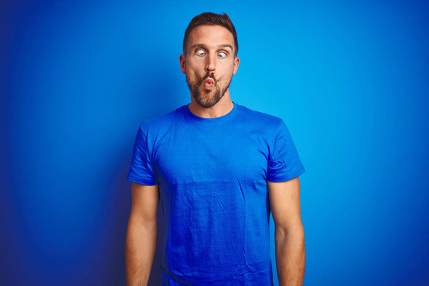 Young handsome man wearing casual t-shirt over blue isolated background making fish face with lips, crazy and comical gesture. Funny expression. - Photo, Image