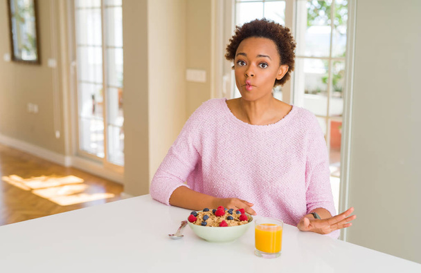 junge afrikanisch-amerikanische Frau, die morgens zu Hause gesund frühstückt und Fischgesicht mit Lippen, verrückter und komischer Geste macht. Lustiger Ausdruck. - Foto, Bild