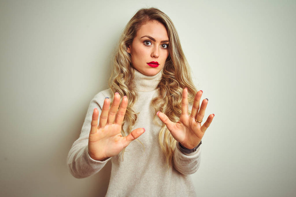 Beautiful woman wearing winter turtleneck sweater over isolated white background Moving away hands palms showing refusal and denial with afraid and disgusting expression. Stop and forbidden. - Photo, Image
