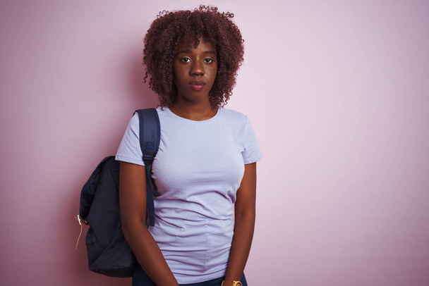 Young african afro tourist woman wearing backpack standing over isolated pink background with serious expression on face. Simple and natural looking at the camera. - Fotografie, Obrázek