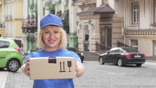 Χαρούμενο παράδοση γυναίκα με μπλε στολή κρατώντας χαρτόνι κουτί - Πλάνα, βίντεο