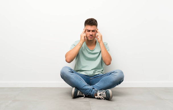 Young handsome man sitting on the floor unhappy and frustrated with something. Negative facial expression - Photo, Image