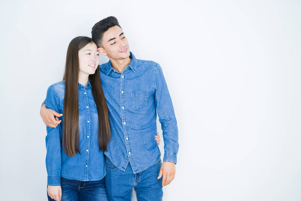 Beautiful young asian couple over white isolated background looking away to side with smile on face, natural expression. Laughing confident. - Фото, зображення