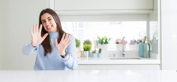 Wide angle picture of beautiful young woman sitting on white table at home afraid and terrified with fear expression stop gesture with hands, shouting in shock. Panic concept. - Фото, зображення