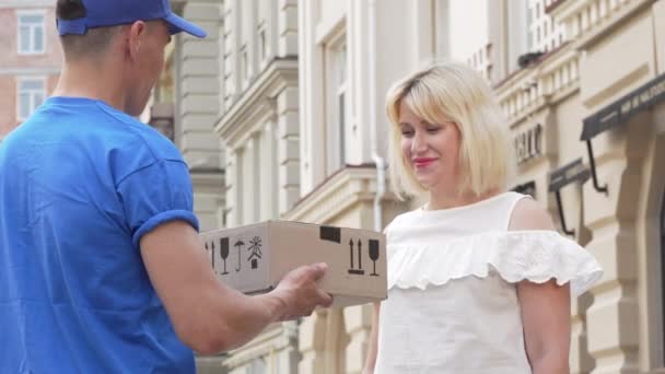 Lovely woman receiving cardboard box parcel from a delivery man - Footage, Video