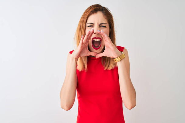 Redhead zakenvrouw dragen van elegante rode jurk staande over geïsoleerde witte achtergrond schreeuwen boos hardop met handen over de mond - Foto, afbeelding