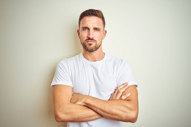Young handsome man wearing casual white t-shirt over isolated background skeptic and nervous, disapproving expression on face with crossed arms. Negative person. - Photo, Image