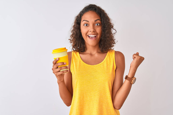 Young brazilian woman drinking take away coffee standing over isolated white background screaming proud and celebrating victory and success very excited, cheering emotion - Photo, Image