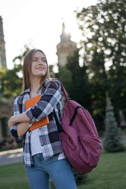 Successful smiling student with backpack and book walking to university. Education concept. Portrait of happy beautiful woman tourist standing outdoors and waiting for taxi - Photo, Image
