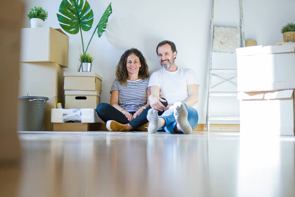 Średnim wieku starszy romantyczna para w miłości siedzi na podłodze w mieszkaniu z kartonów wokół i uśmiechnięty szczęśliwy do przejścia do nowego domu - Zdjęcie, obraz