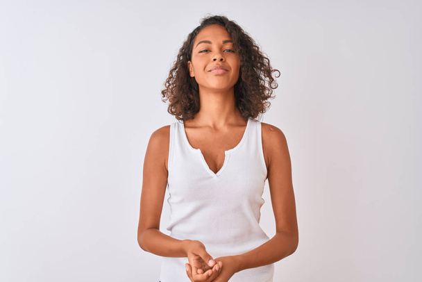 Young brazilian woman wearing casual t-shirt standing over isolated white background with hands together and crossed fingers smiling relaxed and cheerful. Success and optimistic - Φωτογραφία, εικόνα