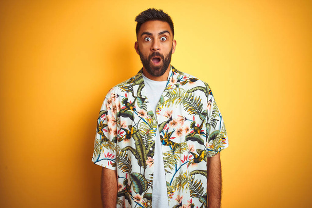 Young indian man on vacation wearing summer floral shirt over isolated yellow background afraid and shocked with surprise expression, fear and excited face. - Foto, afbeelding