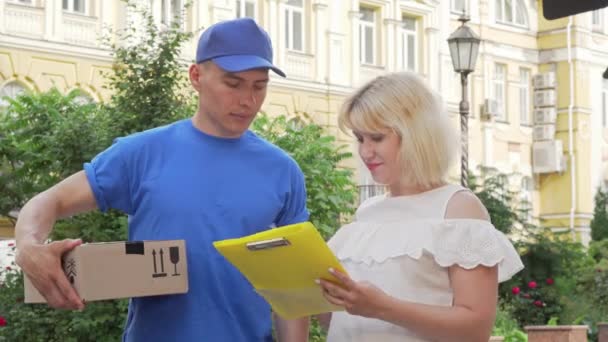 Onnellinen nainen allekirjoitus kuitti ja vastaanottaa paketin kuriiri
 - Materiaali, video