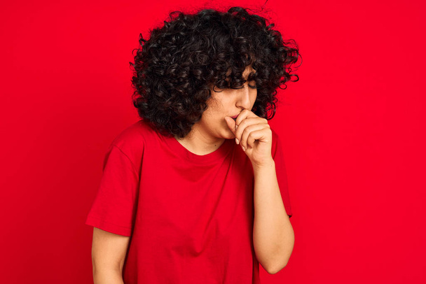 junge Araberin mit lockigem Haar, lässigem T-Shirt über isoliertem rotem Hintergrund, fühlt sich unwohl und hustet als Symptom für Erkältung oder Bronchitis. Gesundheitskonzept. - Foto, Bild