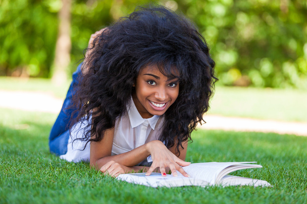 Young student girl reading a book in the school park - African p - Фото, изображение