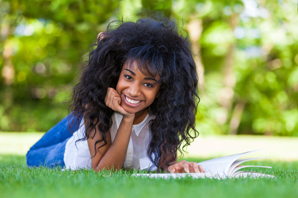 Young student girl reading a book in the school park - African p - Фото, изображение