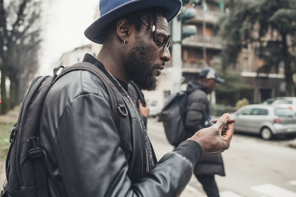 πορτρέτο του νεαρού Αφρικανού που στέκεται στο δρόμο και καπνίζει - Φωτογραφία, εικόνα