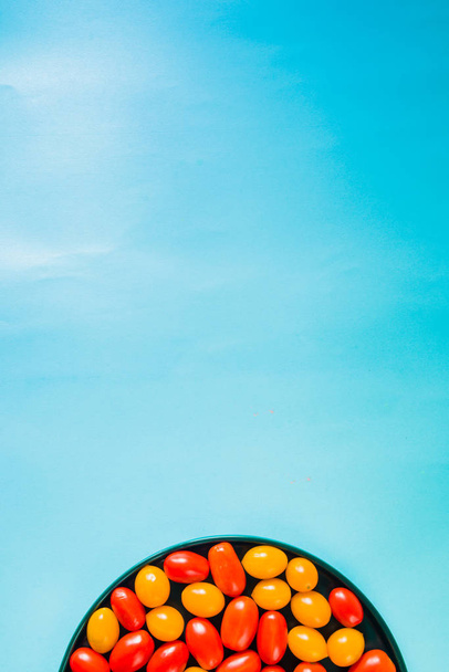 Помідори вишневого кольору на синій тарілці на синьому жирному фоні, вид зверху, природне світло
. - Фото, зображення