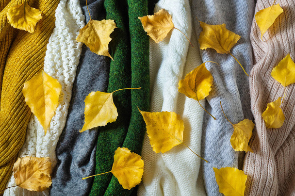 Pile of knitted clothes with autumn leaves, warm background, knitwear, space for text - Photo, Image