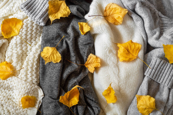 Pile of knitted clothes with autumn leaves, warm background, knitwear, space for text - Zdjęcie, obraz