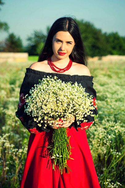 Zdjęcie dziewczyny w polu, haftowane bluzka, ukraiński strój, bukiet kwiatów, chodzić w terenie, czerwone koraliki, kwiaty, Dziewczyna z kwiatami, Ukraińska dziewczyna, czerwona spódnica, czarne włosy, kwiaty, młoda dziewczyna, Dziewczyna w przyrodzie, Dziewczyna w polu, strój - Zdjęcie, obraz