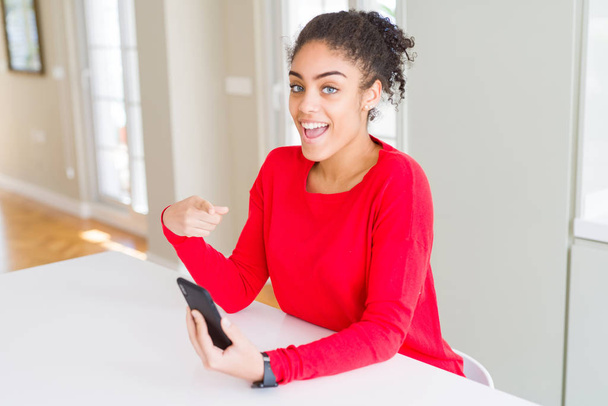 Nuori afrikkalainen amerikkalainen nainen käyttää älypuhelinta tekstiviesti erittäin onnellinen osoittaa käsin ja sormella
 - Valokuva, kuva