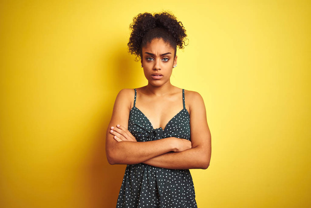 African american woman wearing summer casual green dress over isolated yellow background skeptic and nervous, disapproving expression on face with crossed arms. Negative person. - Photo, Image