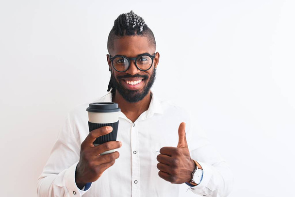 African American biznesmen z warkocze picia kawy na białym tle biały szczęśliwy z wielkim uśmiechem robi OK znak, kciuk w górę z palcami, doskonały znak - Zdjęcie, obraz