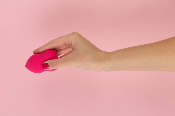Girl hand holds a beauty makeup blender on a pink background, copy space. - Zdjęcie, obraz