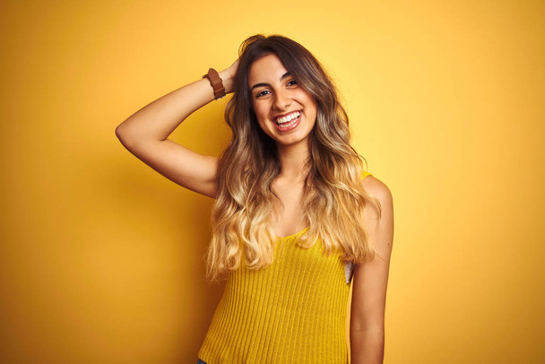 Joven hermosa mujer usando camiseta sobre fondo aislado amarillo sonriendo confiado tocar el cabello con la mano hacia arriba gesto, posando atractivo y de moda
 - Foto, Imagen