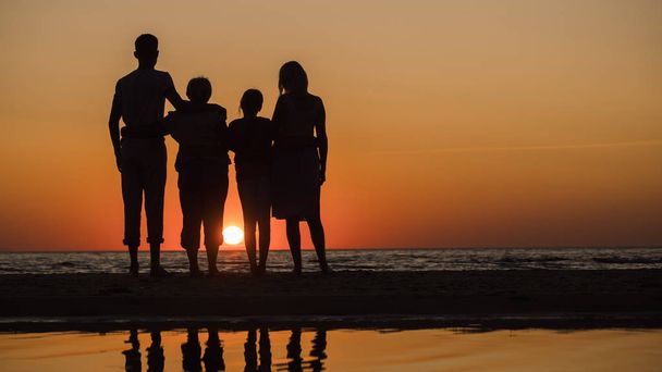 Rodzina z dziećmi i babcia somtry razem o zachodzie słońca nad morzem - Zdjęcie, obraz