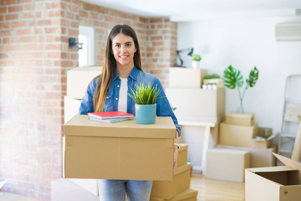 Молодая женщина, держащая картонную коробку в новой квартире,
 - Фото, изображение