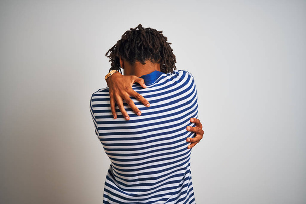 Afro człowiek z dredy ubrany w paski niebieskie Polo stoi na białym tle białe przytulanie się szczęśliwy i pozytywny od tyłu. Self Love i Self Care - Zdjęcie, obraz