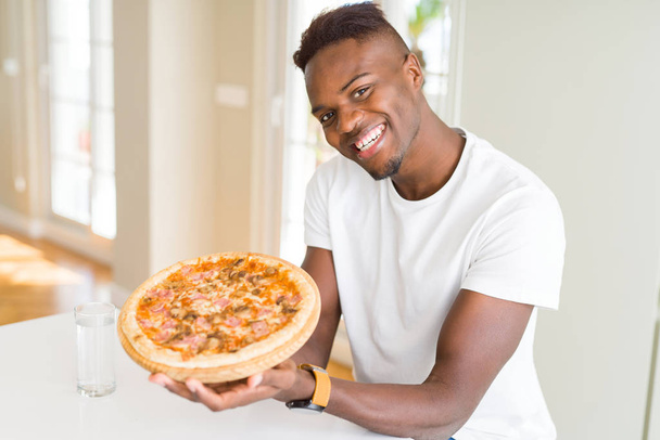 Knappe jonge Afrikaanse man houden en tonen trots zelfgemaakte kaas pizza glimlachen - Foto, afbeelding