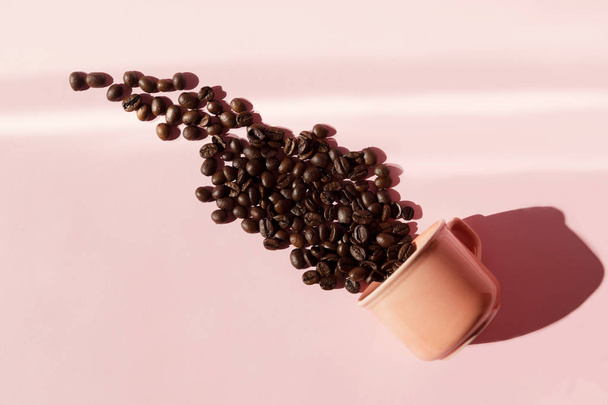 korallenfarbene Tasse mit überschäumenden Kaffeebohnen mit Schatten auf pastellrosa Hintergrund. flach lag. Ansicht von oben. Kaffee-Konzept. Stillleben der Pop-Art - Foto, Bild