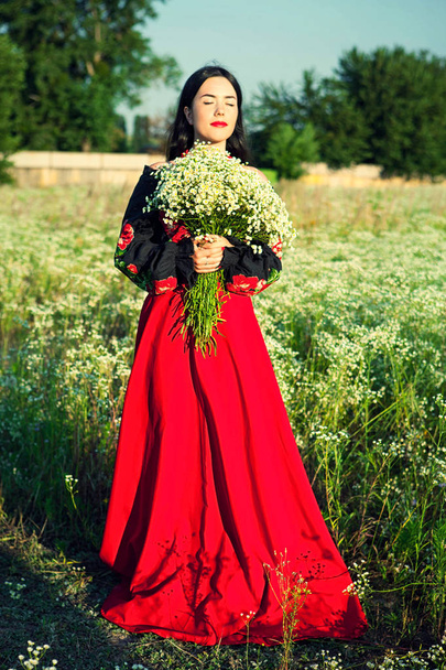 Ukrajinská dívka na poli s kytici květin, dlouhé sukně, rudé sukně, velká kytice, kytice květin, dívky v terénu, květinové pole, divoké květiny, ukrajinská výstroj, vyšívané sako, vyšívané tričko, zavřené oči, portrét dívky,  - Fotografie, Obrázek