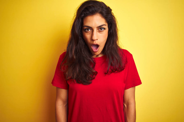 junge schöne Frau in rotem T-Shirt, die vor isoliertem gelben Hintergrund steht, erschrocken mit einem Überraschungsgesicht, ängstlich und aufgeregt mit ängstlichem Ausdruck - Foto, Bild