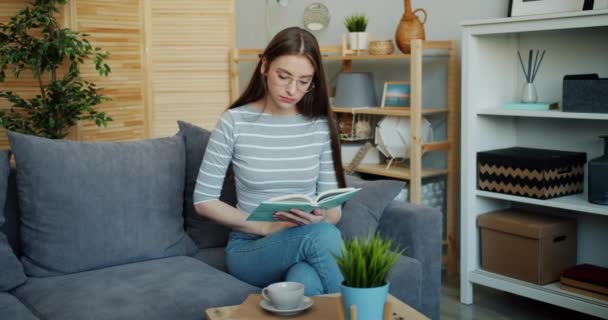 Portrait of serious lady reading book on sofa in apartment focused on activity - Video